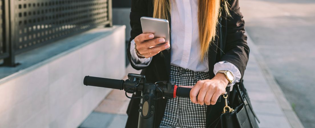 Unrecognizable businesswoman with e-scooter looking at cellphone