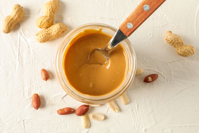 Glass jar with creamy peanut butter and spoon, and peanut on background, space for text and top view