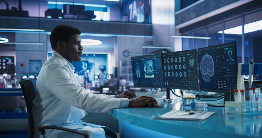 Black Male Neuroscientist Using Desktop Computer To Analyze MRI Scans Of Brain In Medical Research Center Laboratory.