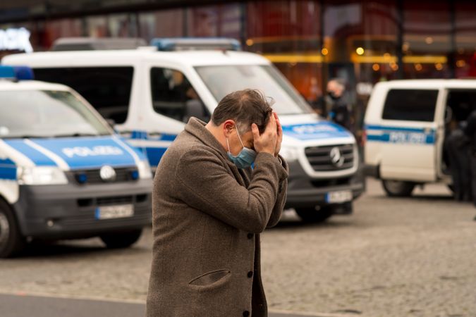 Man with facemask putting his hands on head walking on street