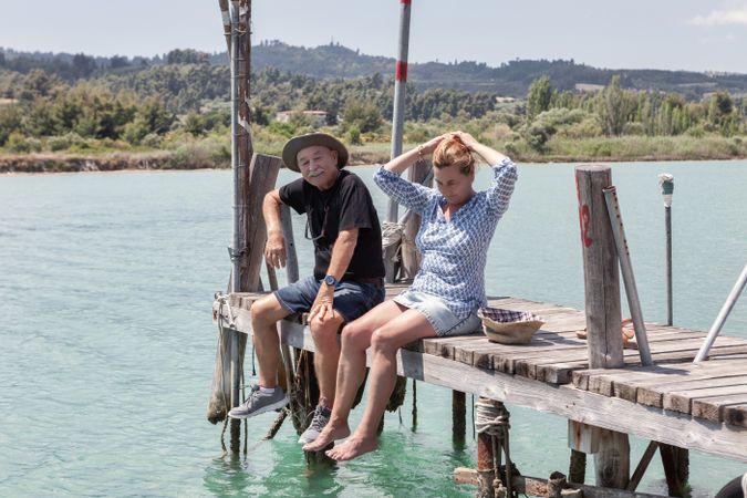 Mature couple sitting on dock dangling with legs
