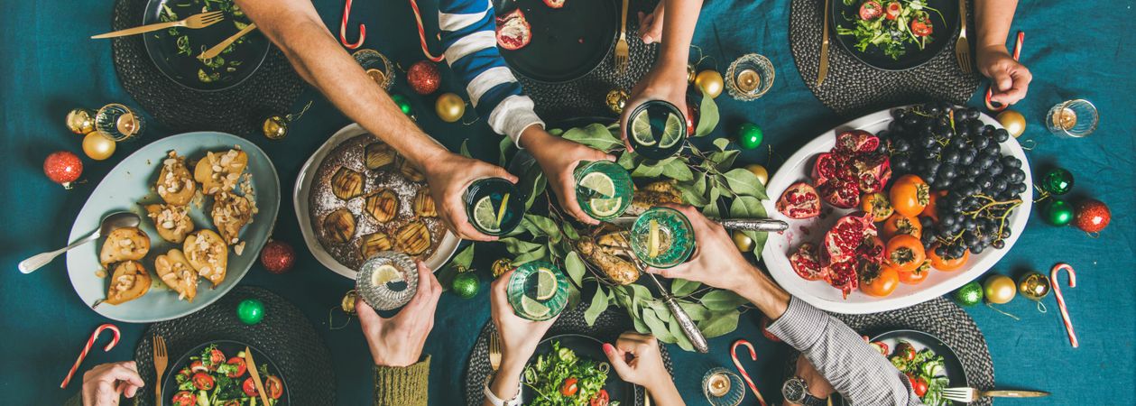 Group toasting at festive table with candy canes and roasted pears, wide composition