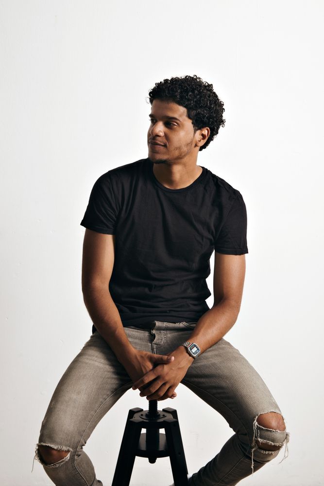 Man in trendy dark clothes sitting on stool and looking away from camera
