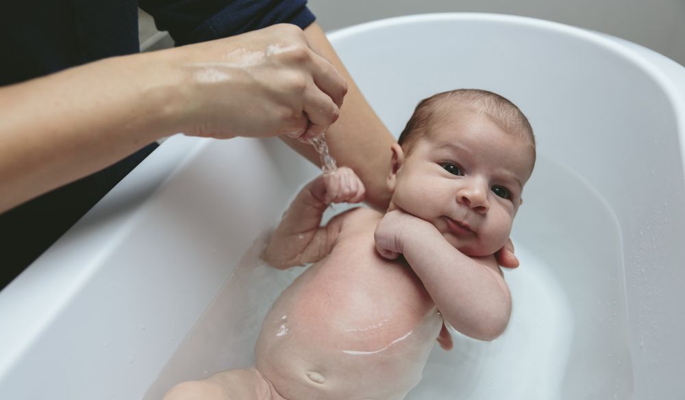 Newborn in the bathtub held by her mother