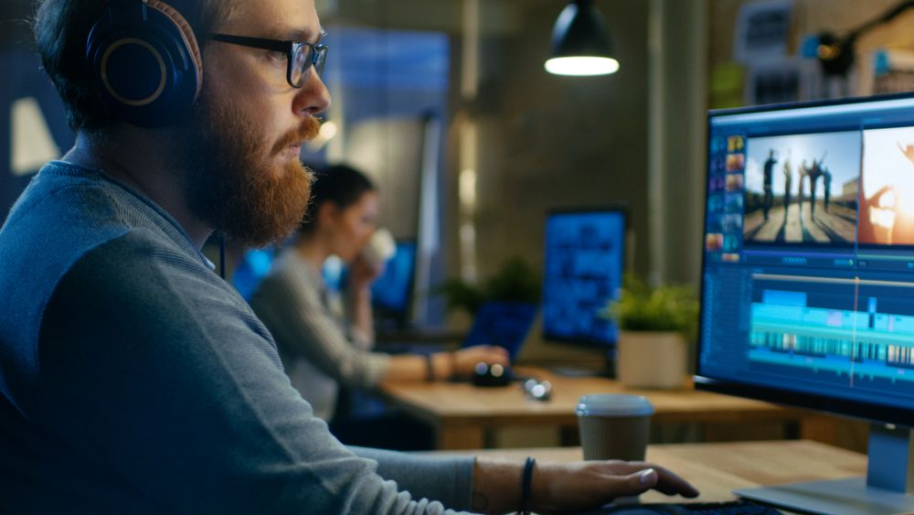 Male Videographer Edits and Cuts Footage and Sound on His Personal Computer, Puts on His Monitors