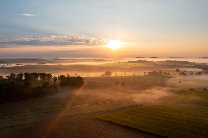 Drone aerial view with foggy agricultural fields at golden hour in the morning