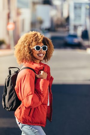 Smiling tourist woman wearing sunglasses and a backpack walking on street