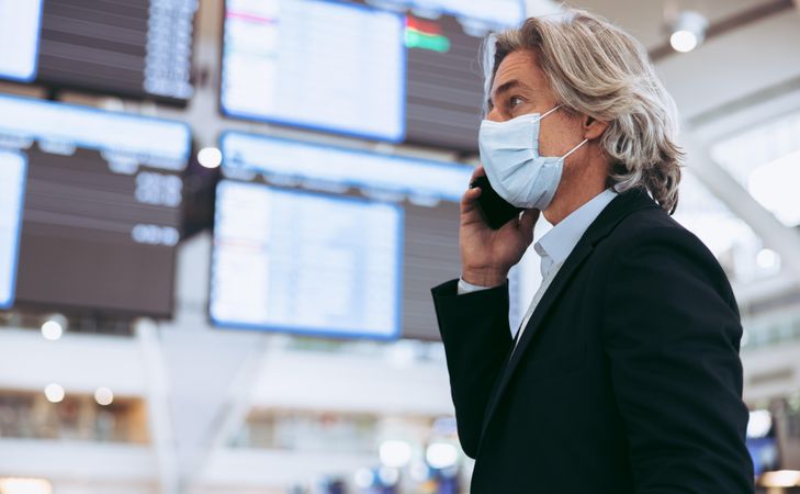 Man with protective face mask talking on cell phone while at airport