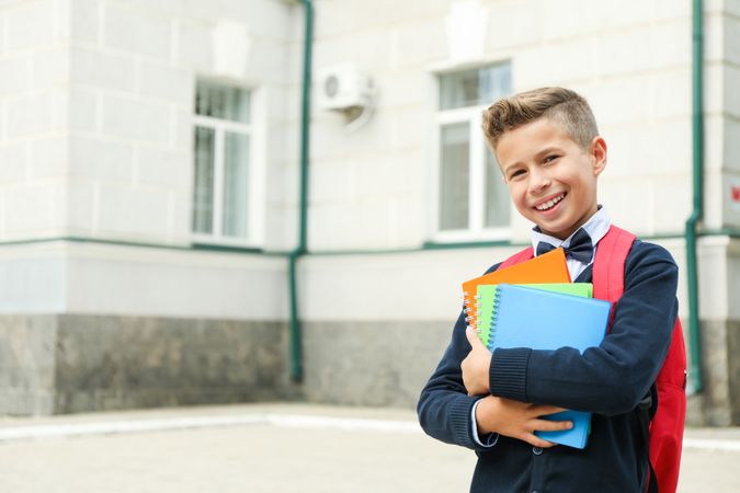 Boy with copybooks against school building, space for text