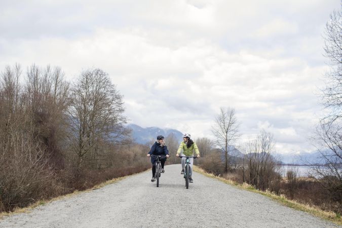 Two women happily talking while riding bicycles around a lake