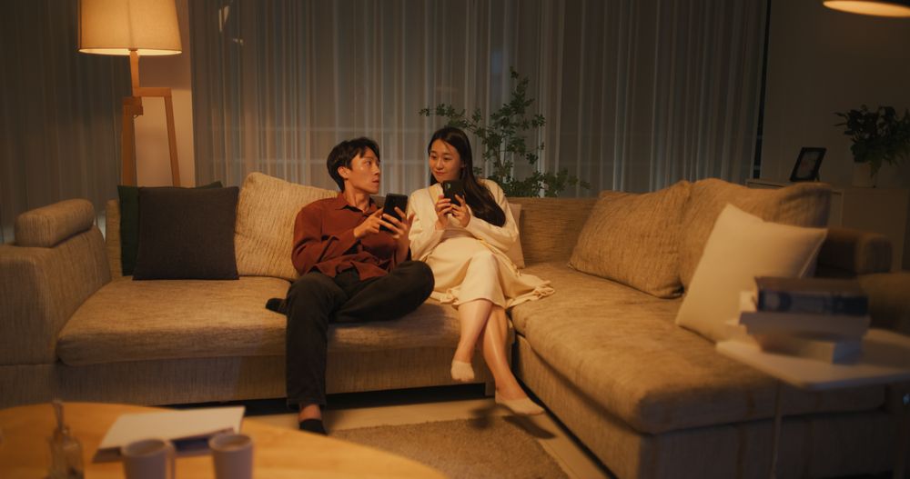 South Korean Couple Using Smartphones While Relaxing on a Couch at Home in a Stylish Living Room
