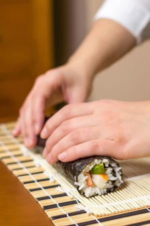 Side view of chef's hand rolling sushi with rice, avocado and shrimps in nori seaweed sheet