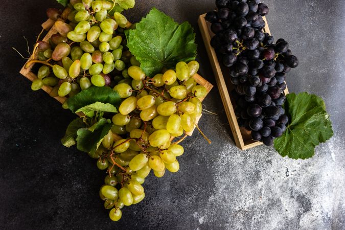 Top view of box of delicious fresh green & red grapes with leaves on counter