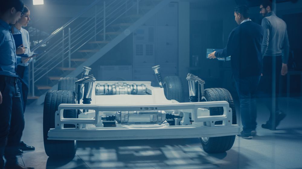 Team of Automobile Design Engineers in Automotive Innovation Facility Working on Electric Car Platform Chassis Prototype that Includes Wheels, Suspension, Hybrid Engine and Battery