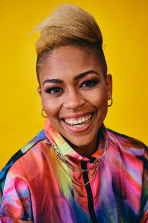 Laughing Black woman in bright 80s windbreaker jacket in yellow studio