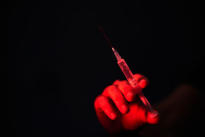 Crop person with syringe in dark room
