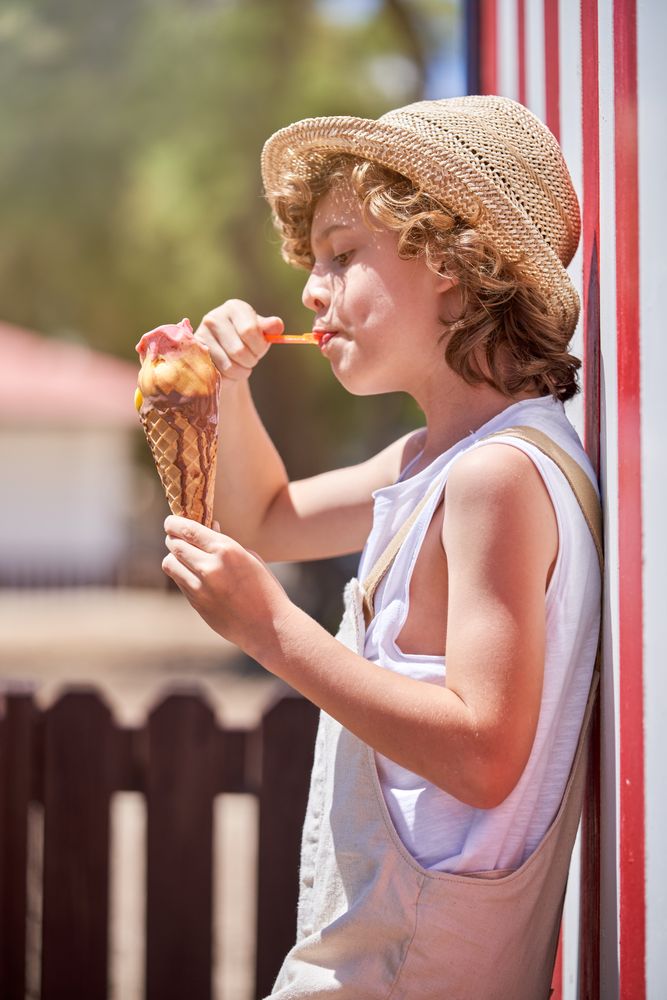 Cute boy in straw hat eating delicious ice cream with syrup