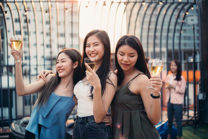 Group of Asian women holding glasses of wine and dancing together
