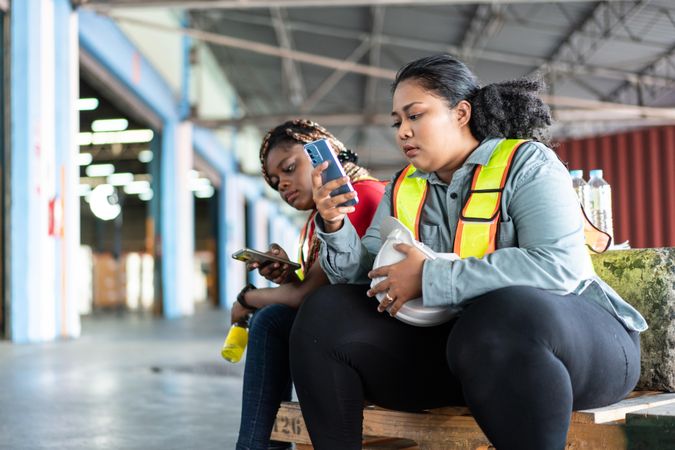 Women in high visibility vests sitting with phone and taking a break from work