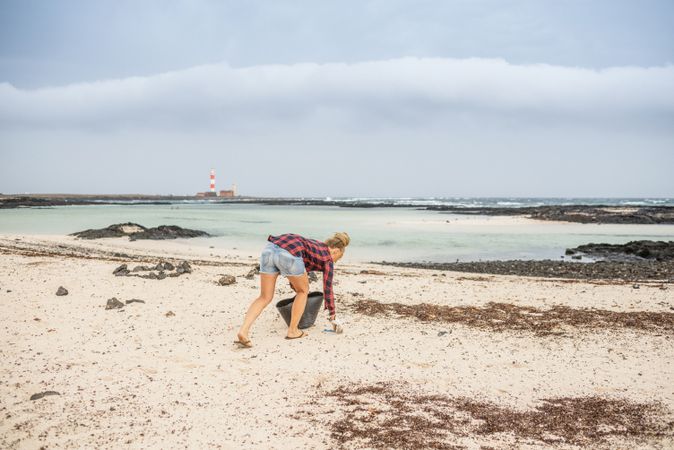 Content modern woman picking litter from sandy seashore
