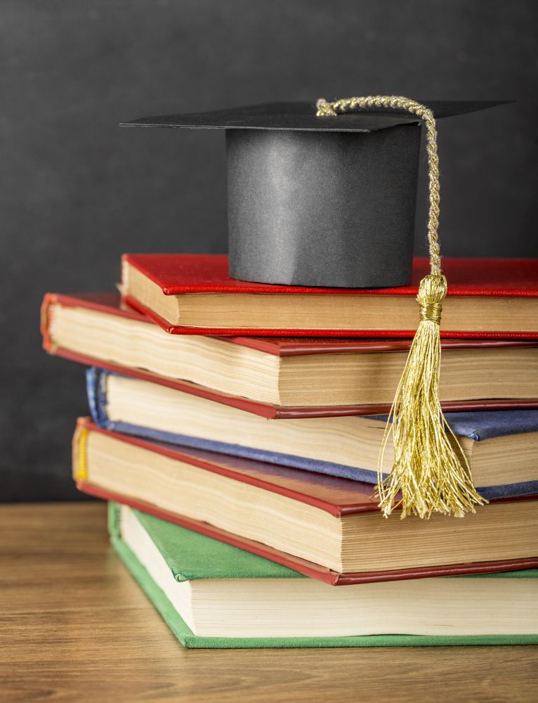 Arrangement of different books with graduation cap