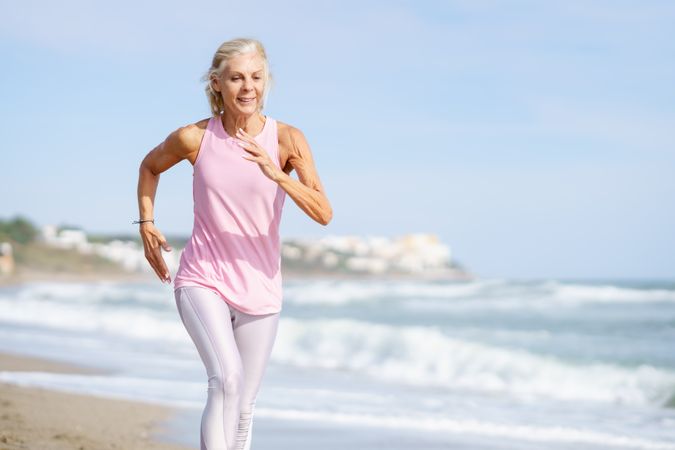 Older woman in sports gear jogging along beach