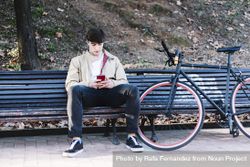 Man sitting on bench outside next to bike checking phone 5r99Bd