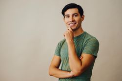 Happy Hispanic male holding his chin in neutral room, copy space