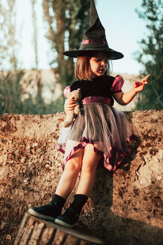 Girl in a witch costumes standing on a wood stump in the forest