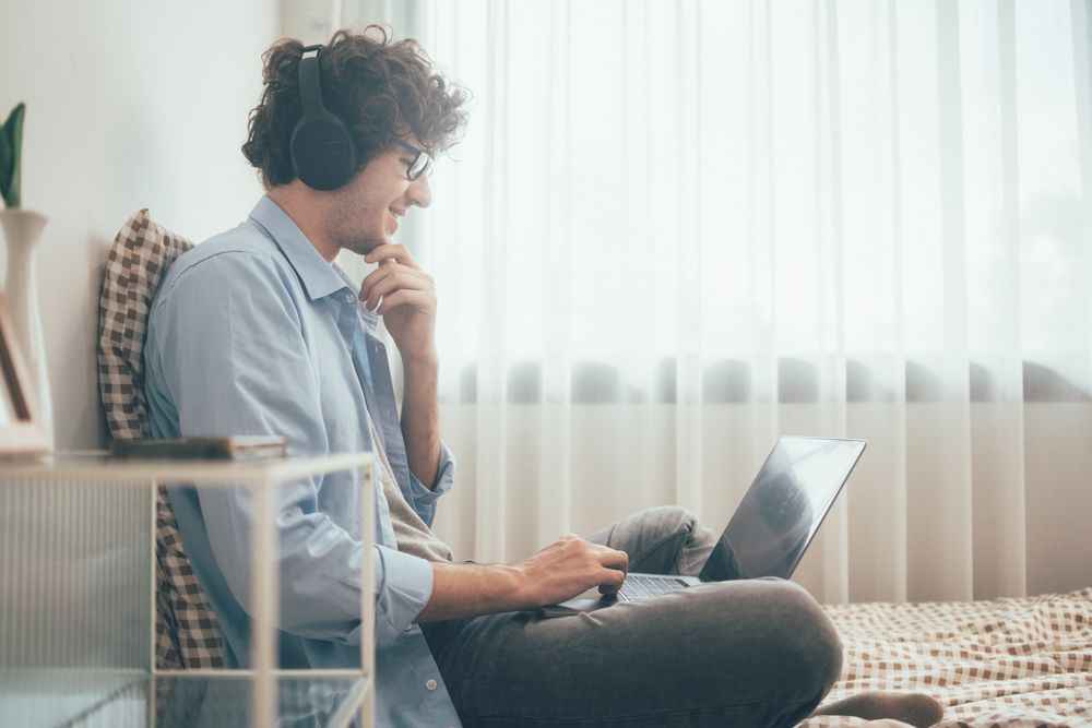 Side view of freelancer listening to music while working on laptop on bed