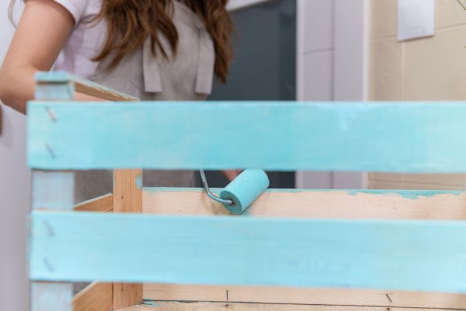 Woman paining wooden box in blue color with roller