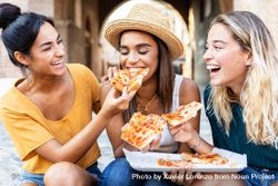 Three cheerful multi-ethnic women eating pizza in the street 4A2ozb