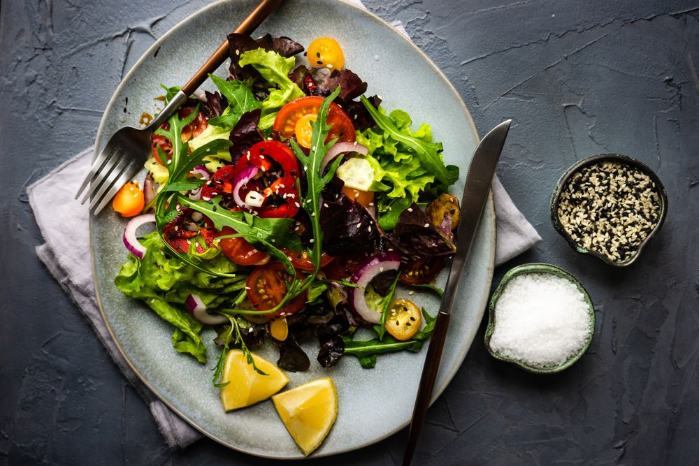 Top view of organic vegetable salad with side of salt and sesame seeds
