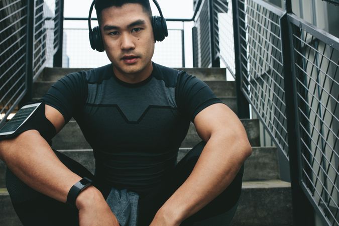 Portrait of asian man relaxing after workout sitting outdoors on stairs