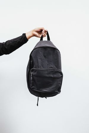 Cropped image of a hand holding a dark backpack against light background