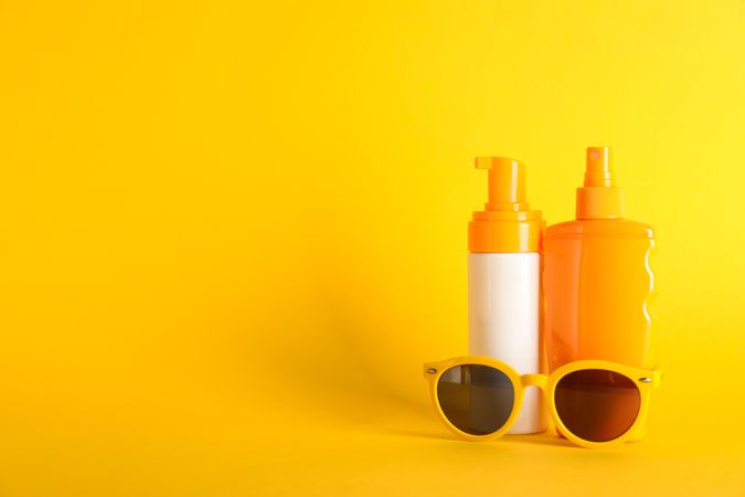 Sunscreen sprays with sunglasses on color background, space for text