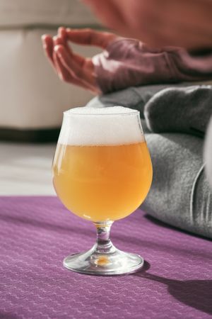 Glass of cold beer near woman on yoga mat