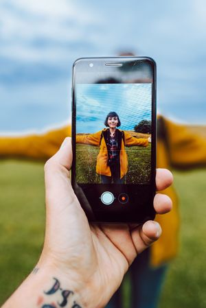 Crop hand taking photo of woman in field