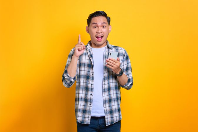 Surprised Asian male pointing up while holding smart phone