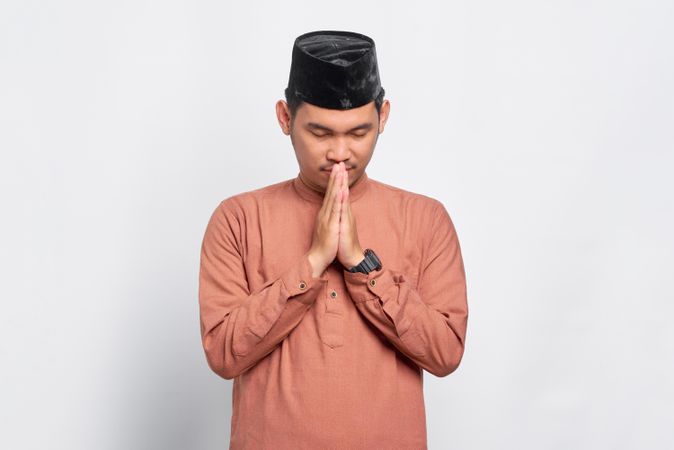 Muslim man in kufi hat with head down in prayer