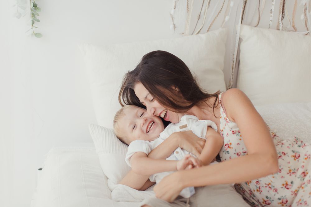 Mother ticking little son and laughing on bed