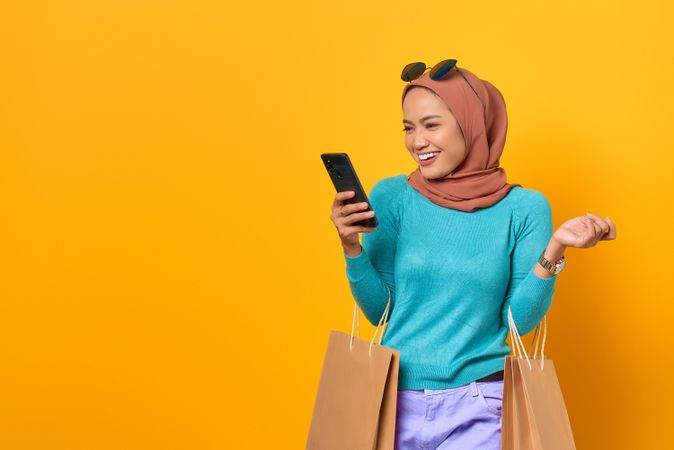 Muslim woman smiling on video call holding shopping bags