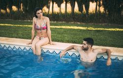 Man swimming and woman sitting on poolside