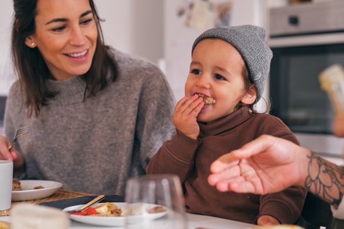 Cheerful girl eating pancake near crop smiling mom