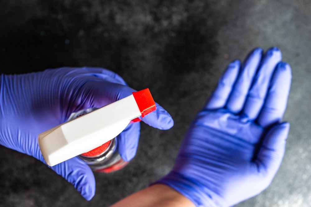 Top view of hands wearing purple latex gloves with spray bottle