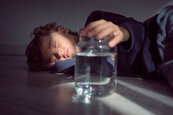 Calm boy in sunlight near glass bottle of water
