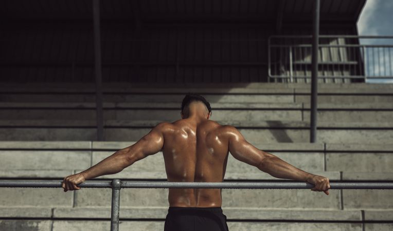 Rear view of athlete standing in stadium with hands on railing