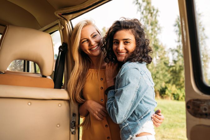 Two female friends posing on an open door to a van