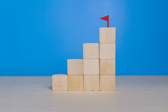 stack staircase wooden blocks with a flag at the top on blue background