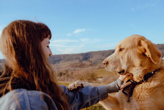 Woman with piercing sitting near dog between field
